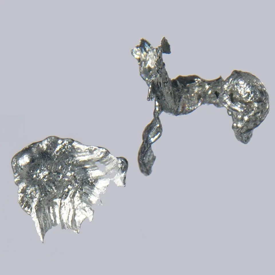 Two irregular pieces of shiny silver-grey cadmium metal on a grey background.