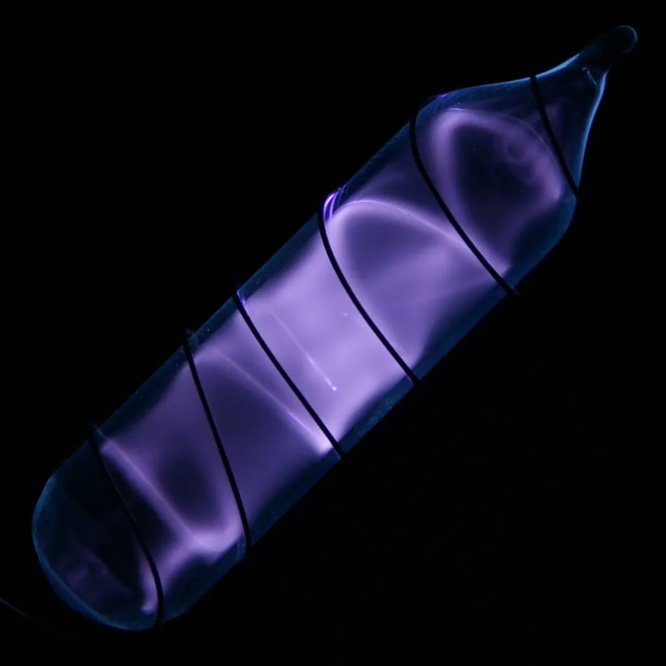 A small glass vial of hydrogen gas glowing violet-pink in an electric discharge, on a black background.
